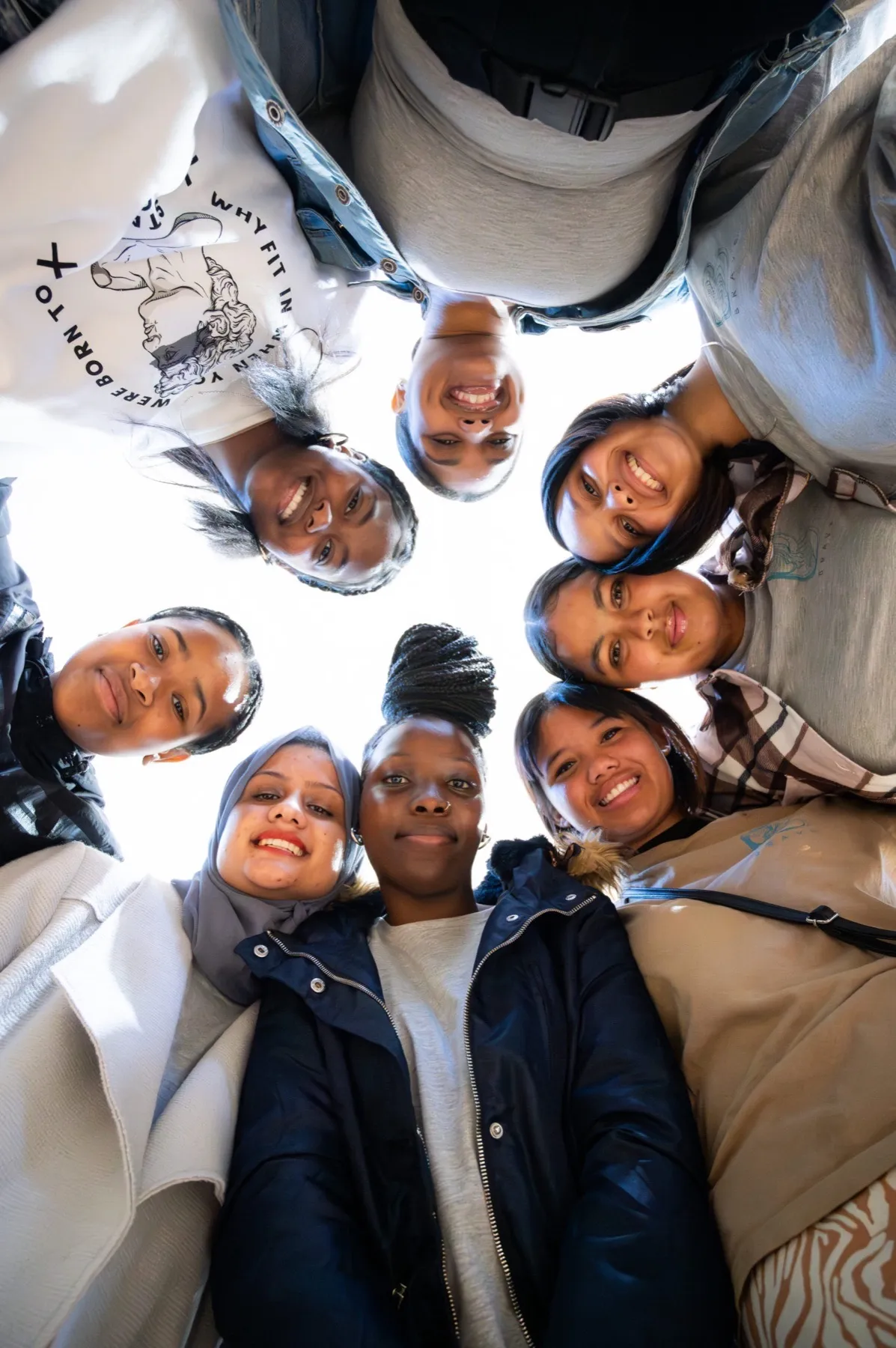 A BRAVE huddle: eight young women in a circle looking up at the camera