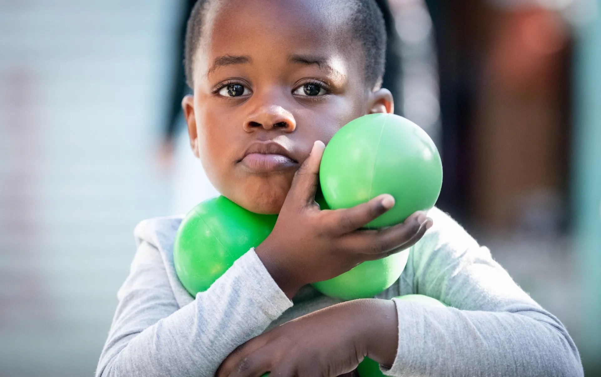 A young boy holding green balls, looking directly at the camera