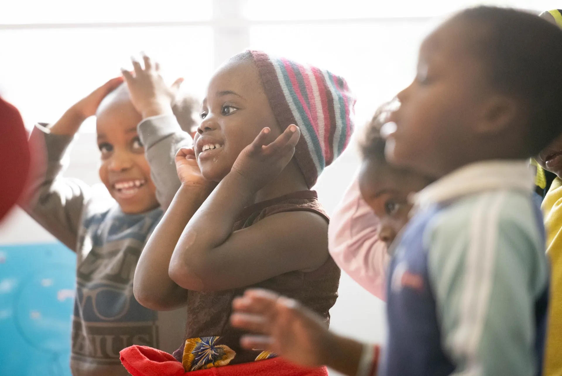 Children dancing with arms raised in a window-lit classroom