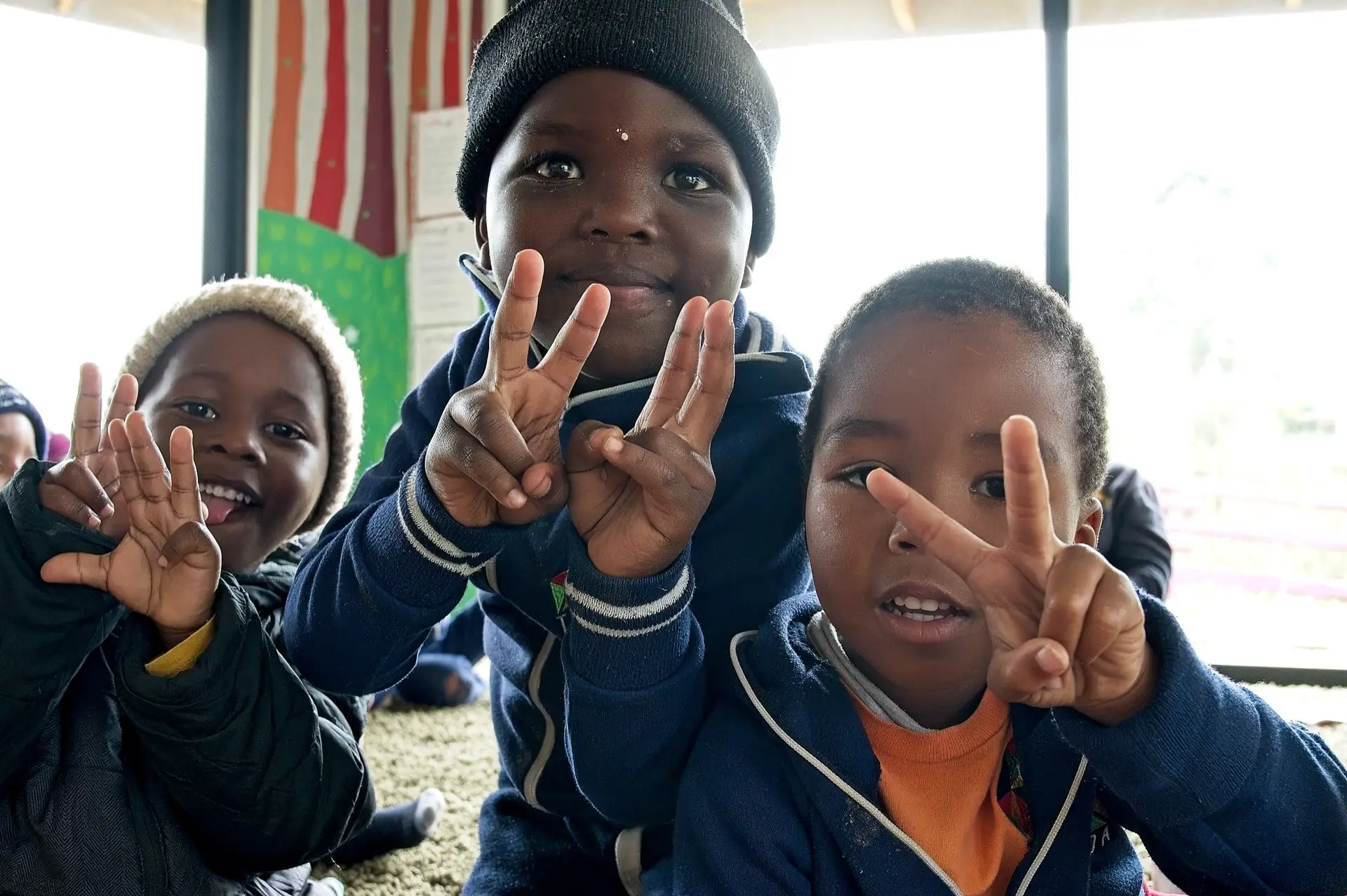 Three children making peace signs and smiling at the camera