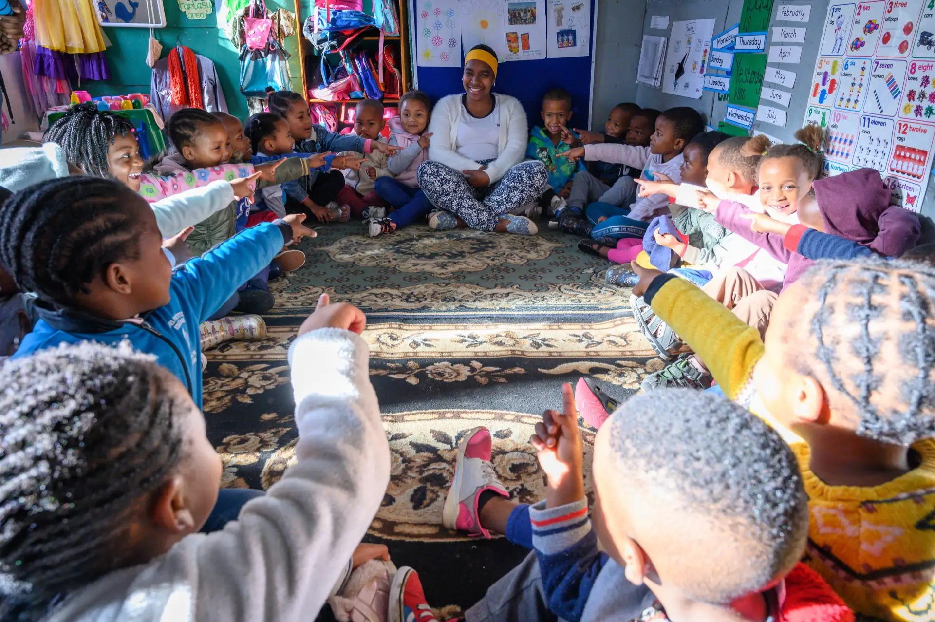 A circle of young children pointing inward during a lesson