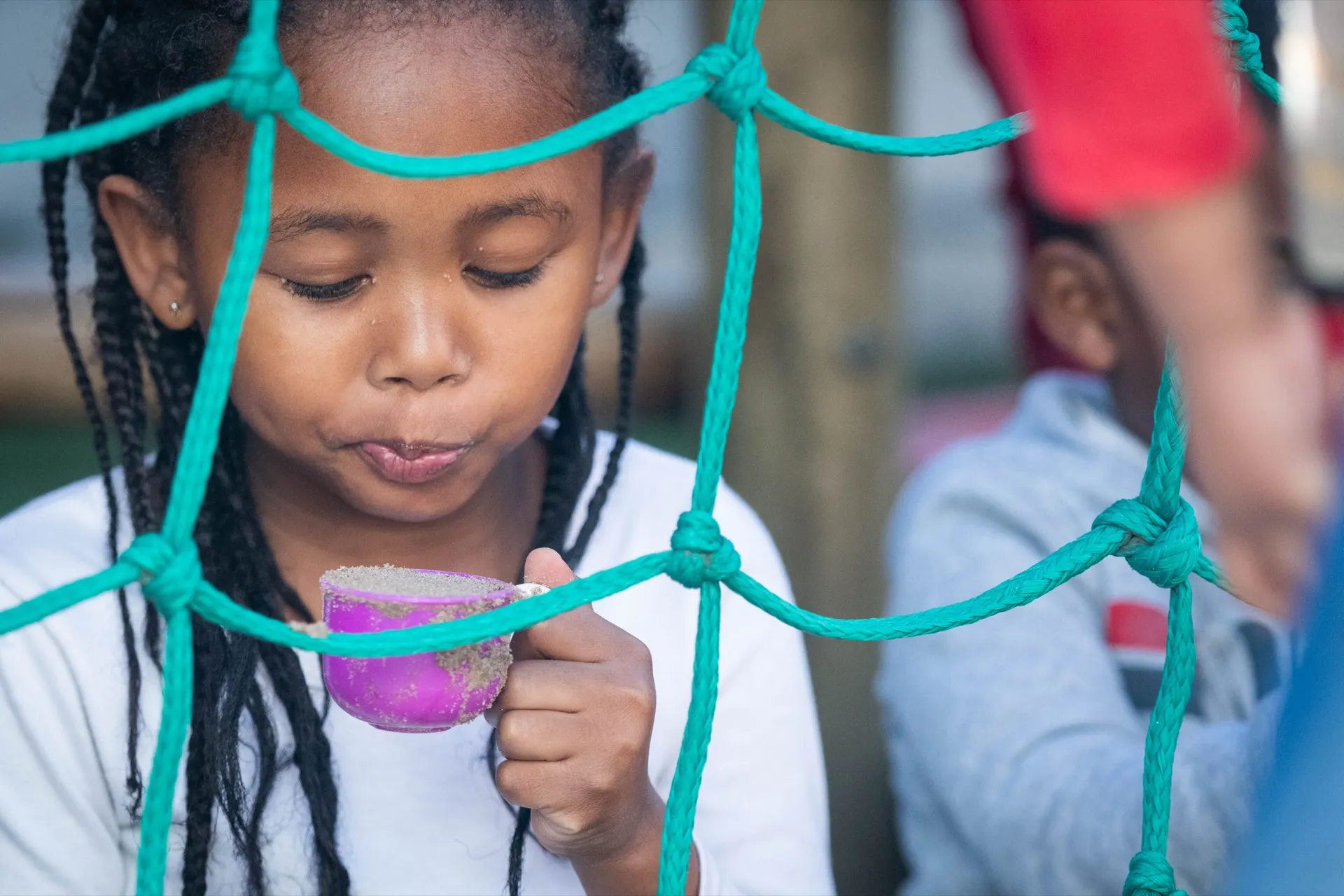 A girl drinking through a climbing-net frame