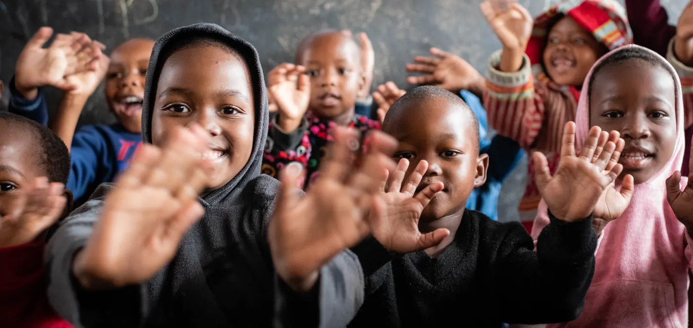 Young children at Siyabonga hold their hands up to the camera in front of a chalkboard