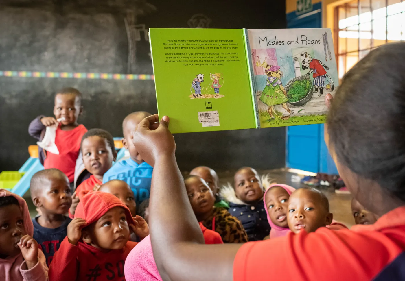 An adult holds up a picture book to a group of young children at Siyabonga