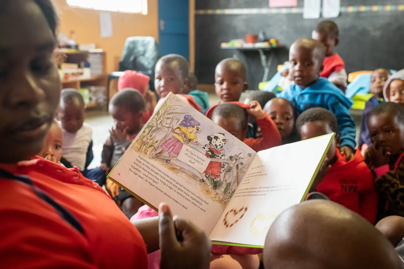 An adult at Siyabonga holds up an open picture book for a classroom of young children sitting on the floor