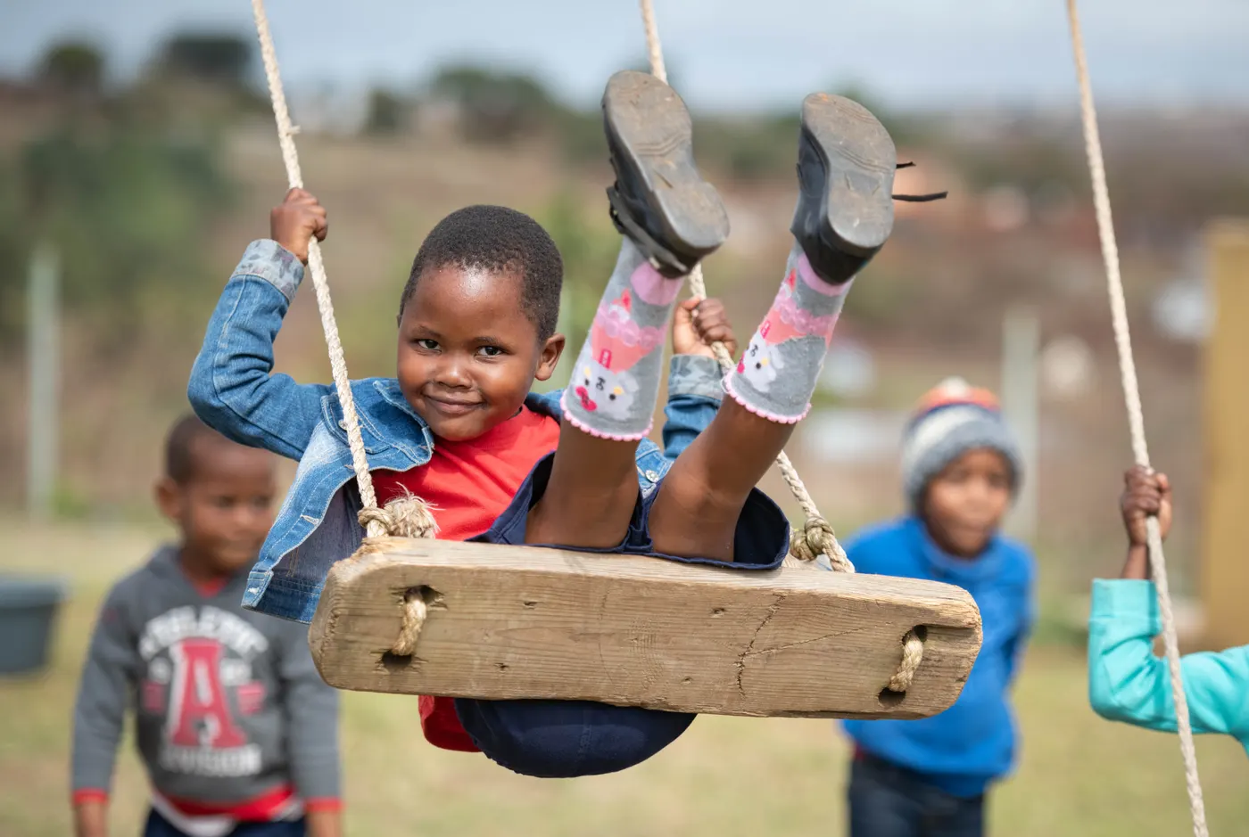 A child at Siyabonga swings on a wooden rope swing, with other children nearby