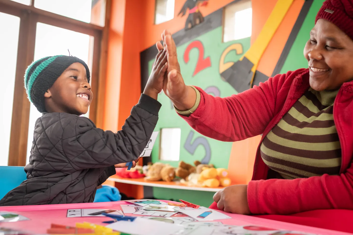 A Thanda teacher and a young boy sharing a high-five over a learning game