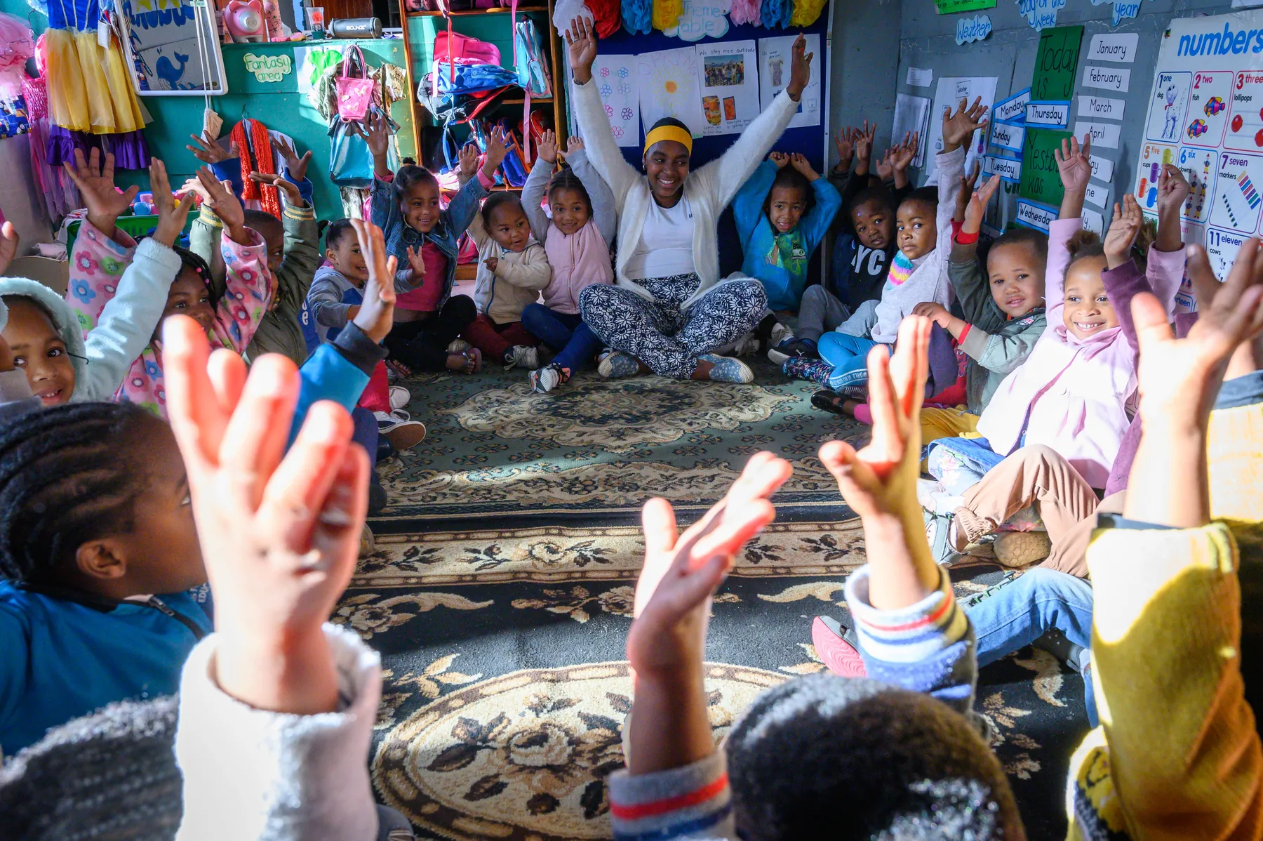 A True North practitioner leading a circle of young children with their arms raised
